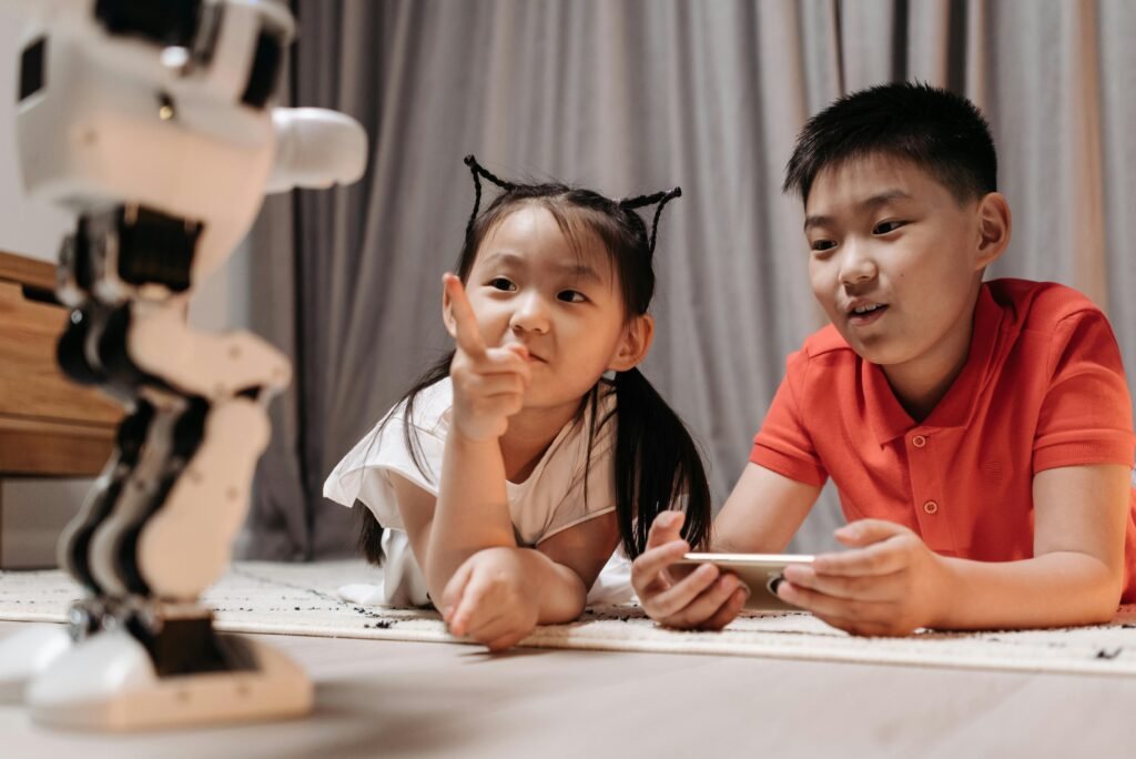 pexels-photo-8294799-8294799 Two children interact with a robotic toy while using a smartphone, showcasing modern technology indoors.